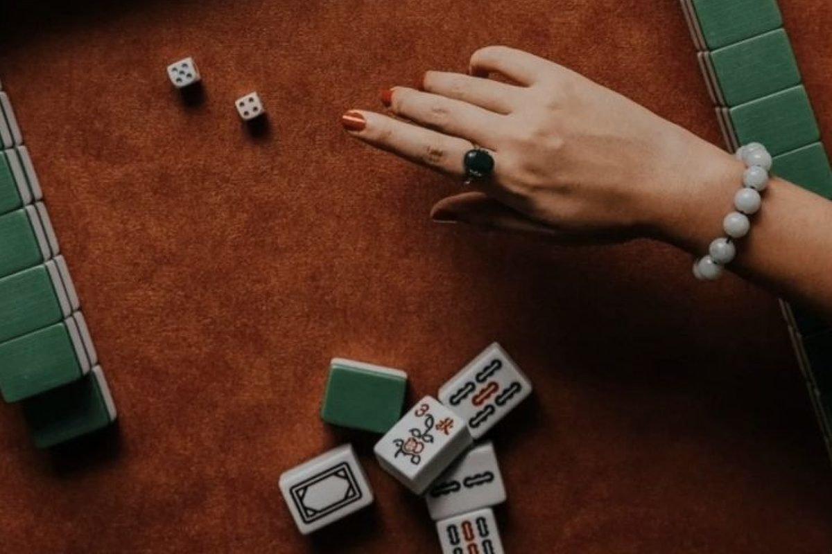 A hand reaching across a felt mahjong table, dice and a cluster of face-up tiles in front of it