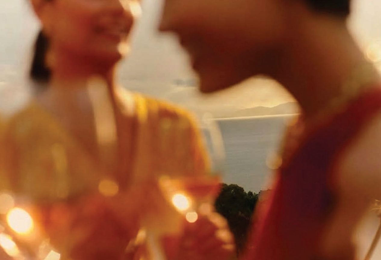 Two members talking over cocktails at golden hour, the water and headlands behind them